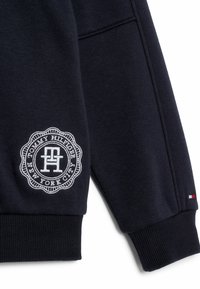 Sudadera azul marino de mezcla de algodón, con un parche de logo bordado en blanco con borde circular y puños acanalados en las mangas.