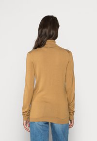 Pull à col roulé à manches longues, de couleur caramel, en tissu tricoté doux. Présente une silhouette ajustée et des poignets côtelés.