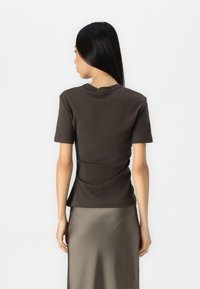 T-shirt marrone scuro a maniche corte con colletto rotondo, texture liscia, forma aderente e design semplice, abbinato a una gonna di raso.