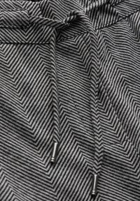 Gros plan sur un tissu gris avec un motif chevron noir et deux cordons noirs munis d’embouts métalliques argentés.