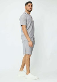 Chemise à manches courtes grise avec un motif texturé, associée à un short assorti. Portée avec des baskets blanches. Design simple et décontracté.