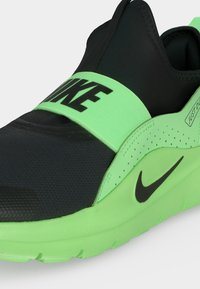 Μαύρο και νέον πράσινο sneaker τύπου slip-on της Nike με ελαστικό λουράκι στην κορυφή που εμφανίζει το "NIKE" με έντονα γράμματα και μαύρο λογότυπο Swoosh στο πλάι.