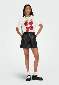 Un t-shirt blanc avec quatre tomates rouges aux contours noirs. Un short en simili cuir noir avec des plis. Les accessoires comprennent un collier en chaîne doré.