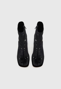 Bocanci negri până la gleznă din satin, cu o textură netedă, care prezintă embellishments cu stele argintii și un fermoar lateral. Design cu bot pătrat.