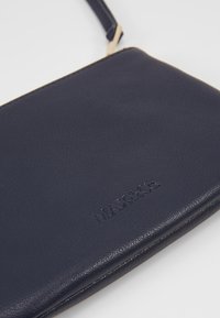 Sacoche en cuir bleu marine avec une texture lisse, dotée d'un logo en relief et d'une tirette dorée. Forme rectangulaire compacte.