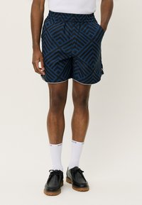 Scurturi bleumarin cu un model geometric în nuanțe închise de albastru. Prezintă un brâu elastic și o bordură albă pe margini.