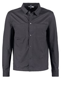 Mustat nappipaitapusero, joka on valmistettu sileästä kankaasta ja jossa on kaksi rintataskua, säännöllinen kaulus ja napitus. Yksinkertainen, selkeä muotoilu.