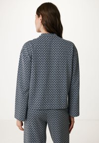 Blå och vit mönstrad jacka med långa ärmar, rundad krage och lös passform. Tyget har en texturerad yta och geometrisk design.