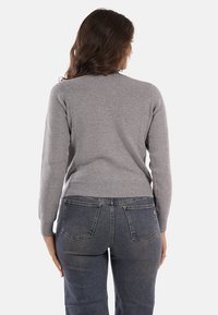 Maglione grigio a maglia con un design aderente. Presenta un collo rotondo e polsini a costine. Indossato con jeans in denim blu scuro. Tessuto testurizzato.