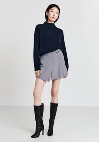 Maglione a collo alto di colore blu navy, pantaloni corti grigi a pieghe e stivali neri alti fino al ginocchio. Tessuto morbido con vestibilità comoda, dettagli in vita accentuati sui pantaloni.