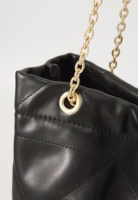 Sac en cuir noir avec une finition matelassée, présentant une bandoulière en chaîne dorée et un détail de œillet doré à l'ouverture.