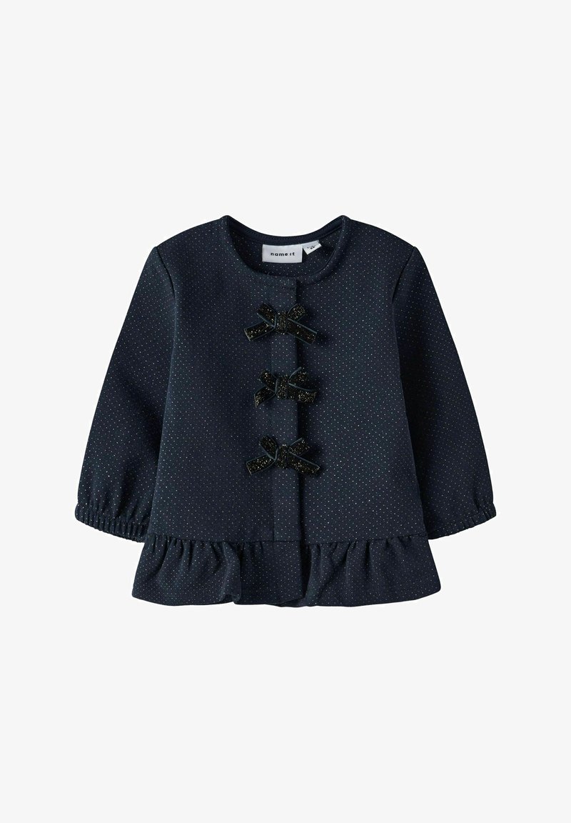 Top de manga larga color navy con lunares blancos, dobladillo con volantes, escote redondo y tres lazos decorativos negros en la parte delantera. Textura suave.
