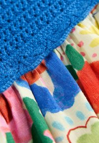 Haut en crochet bleu avec une finition texturée, associé à une jupe à motifs floraux multicolores dans des nuances de rose, vert et bleu.