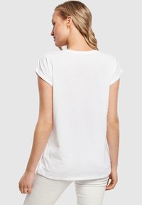 Weißes Baumwoll-T-Shirt mit umgeschlagenen Ärmeln, lässiger Passform und abgerundetem Saum, von hinten vor einem schlichten grauen Hintergrund präsentiert.