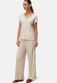 Outfit casual beige chiaro composto da una maglietta a maniche corte con scollatura a V e dettagli testurizzati, abbinata a pantaloni a gamba larga. Tessuto liscio e morbido.