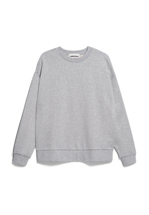Personne portant un sweat-shirt gris clair ample et un pantalon de jogging assorti, les mains dans les poches sur fond blanc.