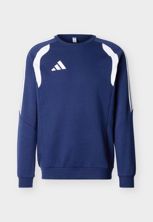 Tumesinist värvi pika varrukaga spordipluus valgete kaarekujuga õlaaktsentide ja kolme valge triibuga varrukatel, esiküljel vasakul rinnal logo.