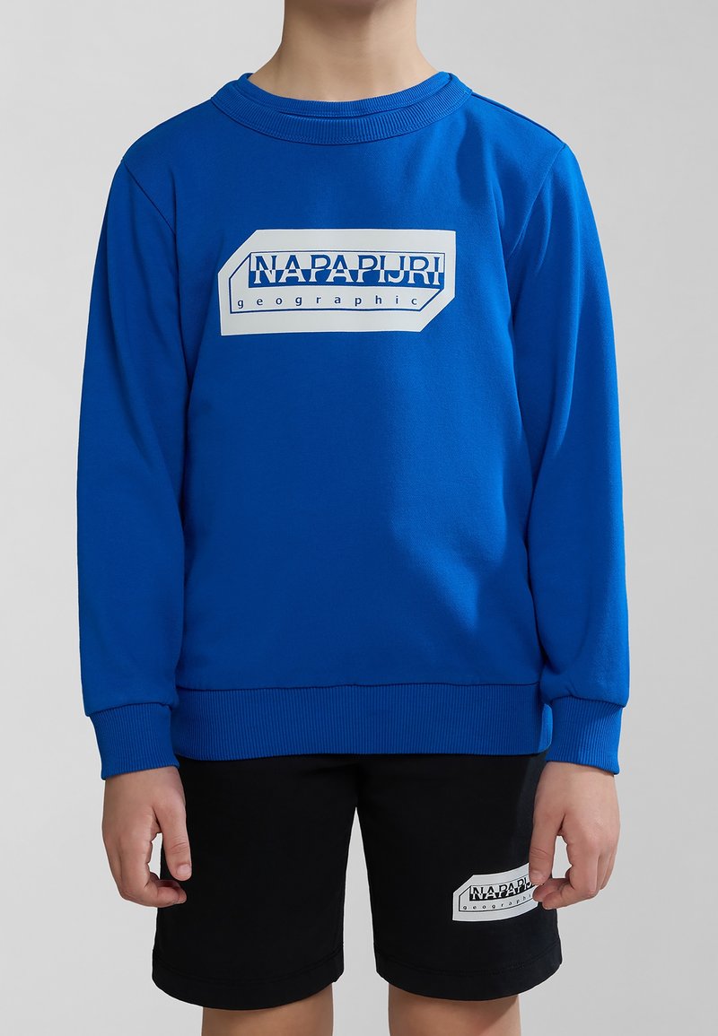 Felpa blu con polsini e orlo a costine, caratterizzata da un logo rettangolare bianco sul davanti. Abbinata a pantaloni corti neri con logo simile.