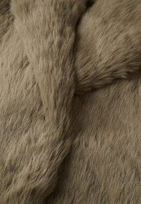 Gros plan d'une texture de fourrure douce, dense et brun clair avec de fines mèches et des variations naturelles de couleur et de direction.