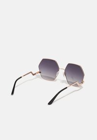 Ochelari de soare hexagonali cu lentile întunecate gradate, cadru din metal de culoare roz aurie și brațe negre cu un design detaliat în zigzag.