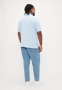 Lyseblå polo med krave, korte ærmer og sideslids, kombineret med afslappede lysvaskede jeans og hvide sneakers.