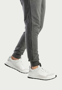 Witte sportieve schoenen met grijze accenten, gemaakt van mesh en synthetisch materiaal, met een gestructureerde zool en vetersysteem, gecombineerd met grijze taps toelopende joggingbroeken.