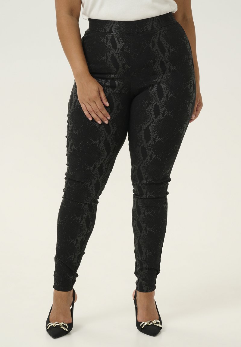 Leggings in stampa serpente nera con una texture liscia, vita alta, vestibilità affusolata, abbinati a décolleté neri con punta a estremo e dettagli in oro.
