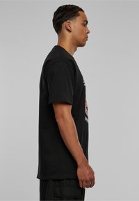Sort bomulds t-shirt med korte ærmer og rund hals, med et farverigt grafisk design på forsiden, set fra siden.