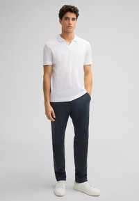 Weißes Poloshirt mit kurzen Ärmeln und Kragen, kombiniert mit marineblauen Chinos und weißen Sneakern, mit lockerer Passform und weicher Textur.