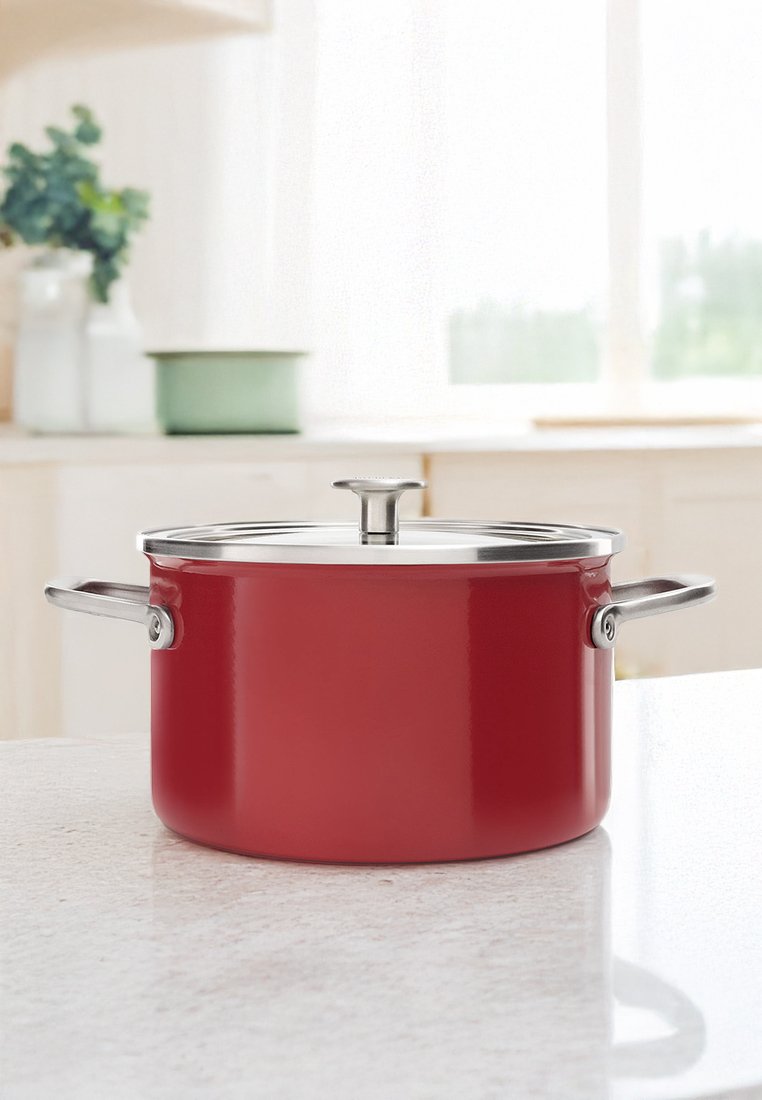 Casserole rouge avec un couvercle en acier inoxydable, dotée de poignées latérales et d'une finition lisse, posée sur un plan de travail en marbre.