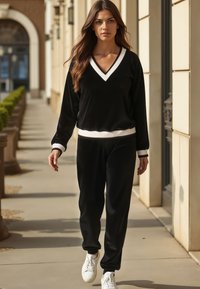 Schwarzes Loungewear-Set in zwei Teilen, bestehend aus einem V-Ausschnitt-Pullover mit weißem Besatz und passenden Hosen, gefertigt aus weichem Stoff mit einer entspannten Passform.