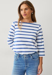 Langsleeve bootcutshirt in het wit met blauwe horizontale strepen. Zachte katoenstof, gecombineerd met lichtblauwe jeans. Eenvoudig ontwerp, casual pasvorm.