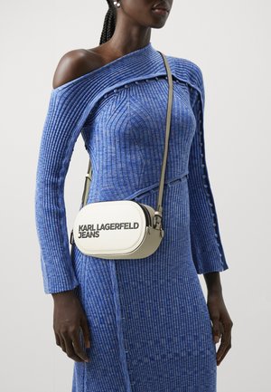 Robe longue à manches longues bleu côtelé avec des détails de boutons, associée à un sac bandoulière ovale blanc portant le texte noir "KARL LAGERFELD JEANS."