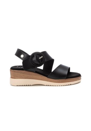 Sandalia cuña de cuero negro con tiras anchas, hebilla redonda, tacón plataforma de madera y suela de goma beige con dibujo acanalado.