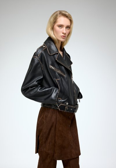 Black leather biker jacket with contrasting tan stitching, featuring a wide collar, side zipper, and front pockets. Paired with a brown suede skirt.