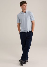 Cămașă polo de culoare albastră deschisă, cu mâneci scurte și guler, asortată cu pantaloni negri închis. Cămașa are un mic logo pe piept.