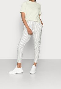 Vaaleanvihreä lyhythihainen t-paita, joka on yhdistetty valkoisiin raidallisiin slim-fit-housuihin ja valkoisiin tennareihin. Asusteet ovat sileän tuntuisia ja rentoa muotoilua.