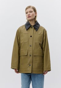 Kaki leren jas met een zwarte kraag, voorzien van twee borstzakken, drie knopen aan de voorkant en een ontspannen pasvorm. Gladde textuur en stevig ontwerp.