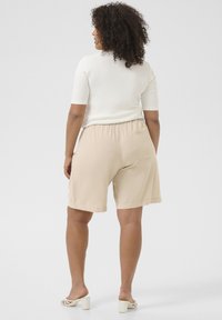 Beige shorts with an elastic waistband and side pocket, paired with a fitted white top. Features a relaxed, knee-length design.