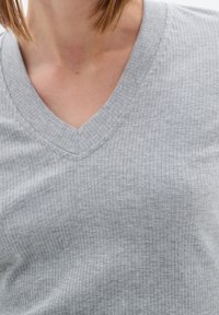 Szary, prążkowany top z dekoltem w serek, wykonany z miękkiego materiału, z teksturowaną powierzchnią i dopasowanym fasonem, który podkreśla dekolt.