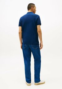 Marineblauwe poloshirt met korte mouwen, gestructureerde stof; blauwe jeans met een klassieke pasvorm, subtiele stiksels en lichtgekleurde sneakers.