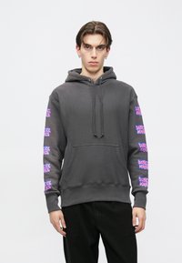 Hanorac gri cu buzunar frontal, glugă cu șnur și imprimeuri grafice roz pe ambele mâneci. Conceput într-o croială lejeră cu manșete drepte.