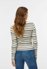 Maglione a righe in crema e nero, texture a coste, design aderente, maniche lunghe, indossato con jeans blu. Vista da dietro.