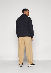 Zwarte fleece pullover met een hoge kraag, gecombineerd met losse beige broek en zwarte sportschoenen; zachte texturen en een relaxte pasvorm.