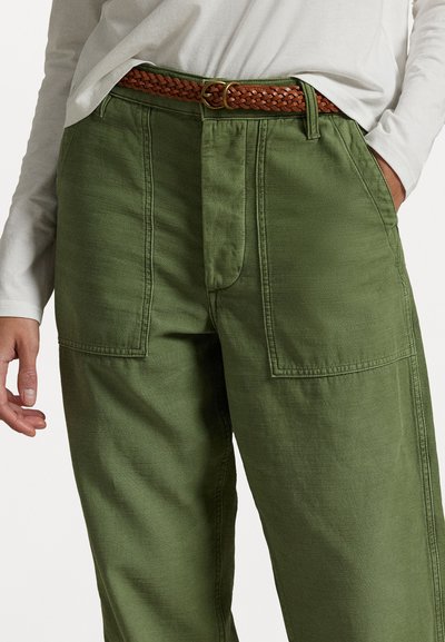 Pantaloni verde oliva con una vestibilità rilassata, dotati di due grandi tasche frontali, cuciture dettagliate e una cintura intrecciata marrone con una fibbia metallica.