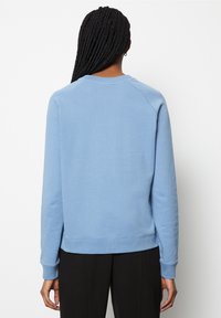 Sudadera azul con cuello redondo y puños acanalados. Material de algodón, textura suave y ajuste relajado. Presenta mangas ranglán y sin logotipos visibles.