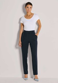 Marineblauwe taillepantalons met een hoge taille, rechte pijpen en zijzakken, gecombineerd met een strak wit T-shirt en lichtblauwe hakken.