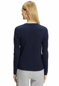 Langarm-Navy-Top aus glattem Stoff, mit Rundhalsausschnitt und geradem Schnitt, getragen mit hellgrauen Hosen.