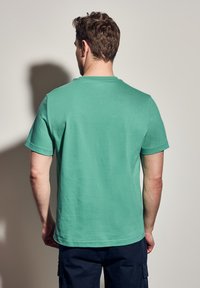 Zelené krátké bavlněné tričko s kulatým výstřihem, hladkým povrchem a rovného lemu, z pohledu zezadu.