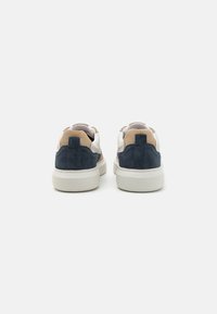 Αθλητικά παπούτσια με σχέδιο από ναυτικό σουέτ και μπεζ λεπτομέρειες, λευκή δερμάτινη πάνω επιφάνεια, μαλακό κολάρο και ελαστική σόλα. Η πίσω όψη δείχνει τις αντίθετες υφές.